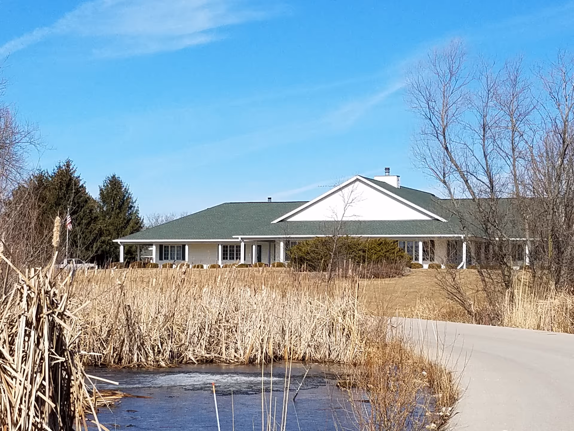 Sage Meadow of Lake Geneva front view: single-story building with green roof, driveway, tall reeds.