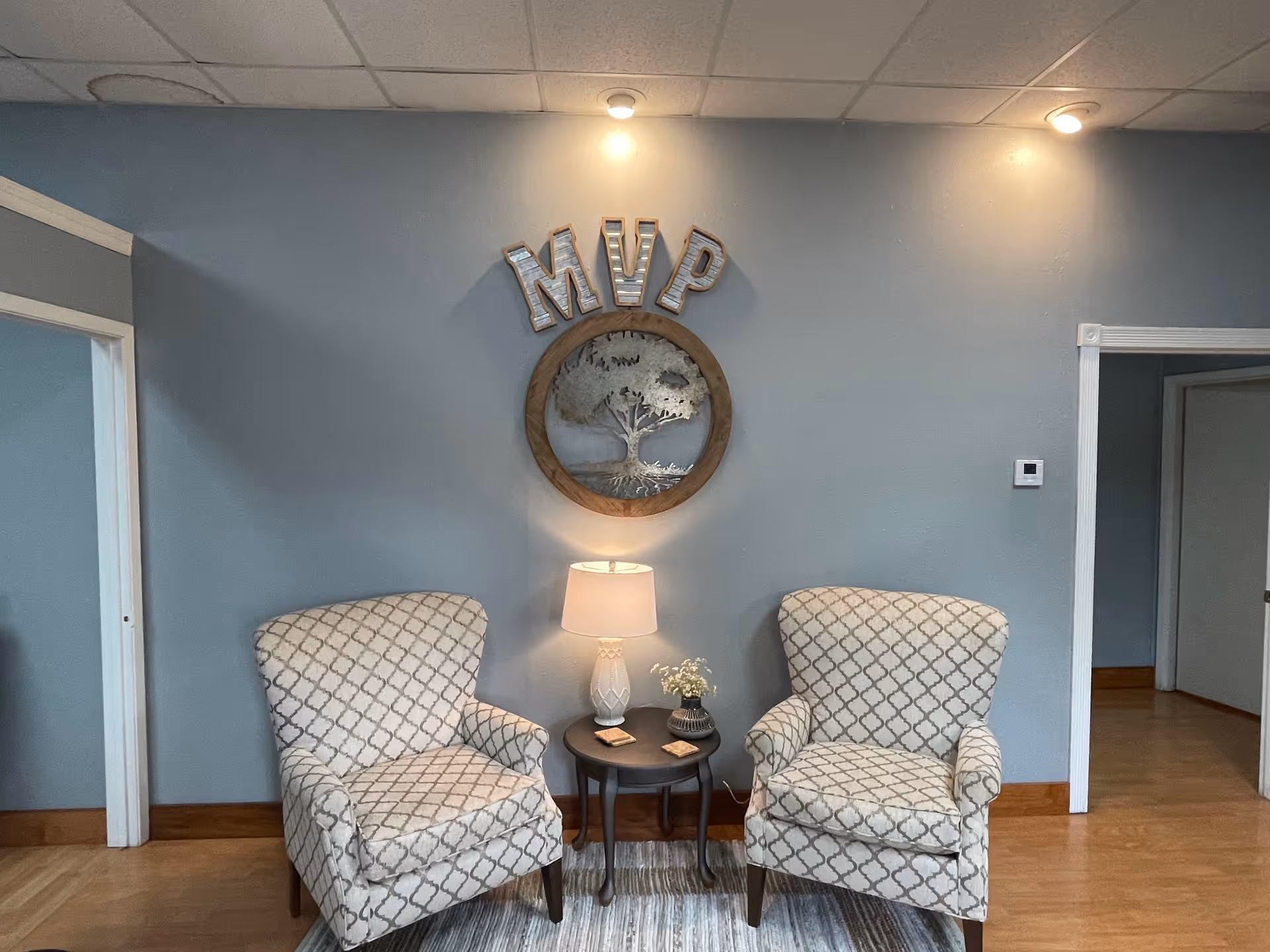 Two patterned armchairs flank a small table with lamp in a blue-walled lounge.