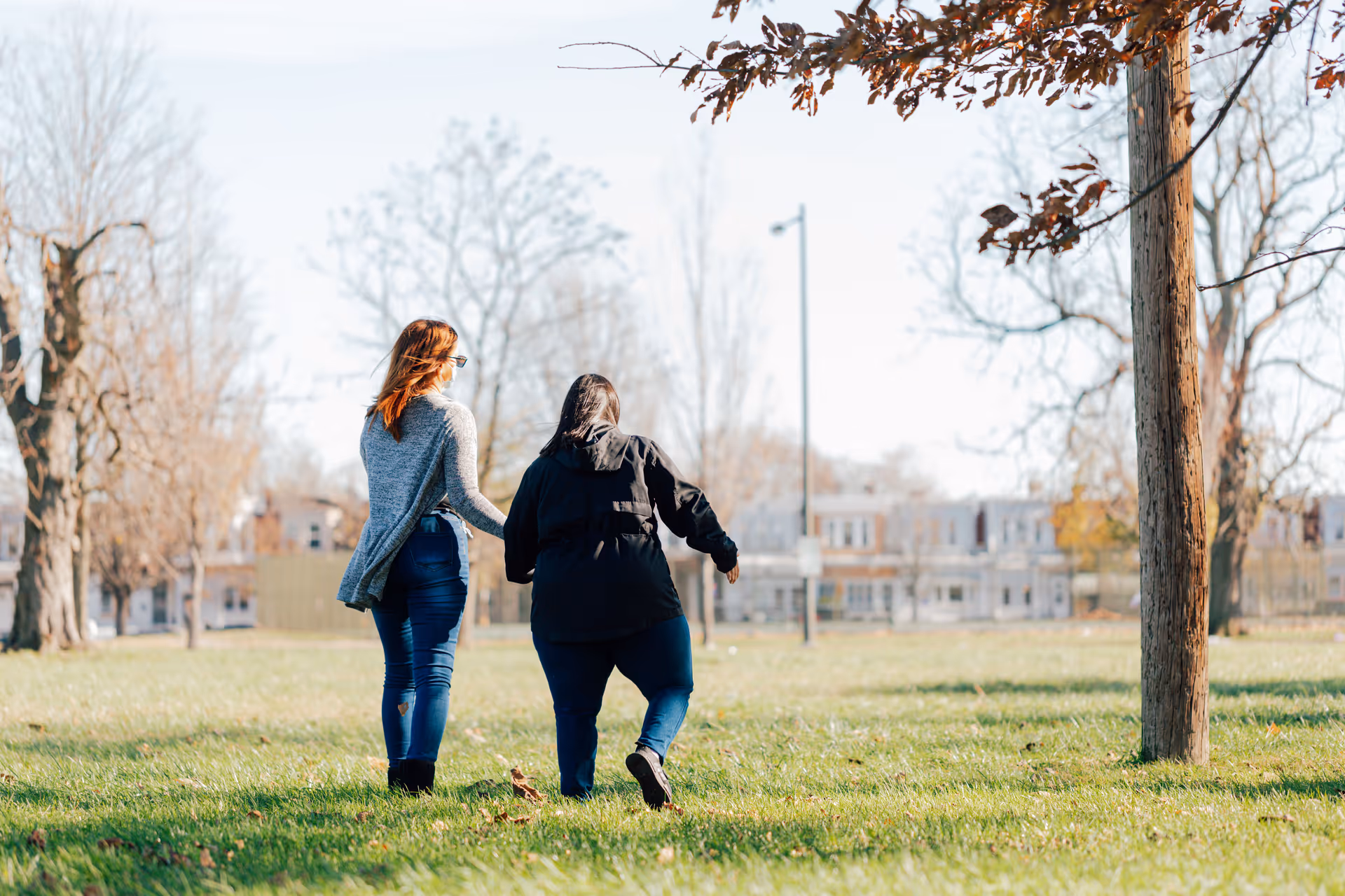 Two people walk across a sunny grassy park near a senior living facility.
