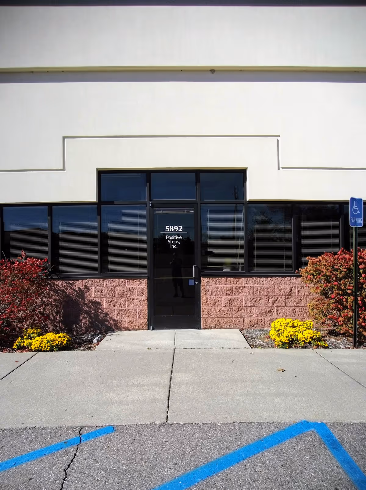 Exterior view of the Positive Steps entrance with glass doors, landscaping, and handicap sign.