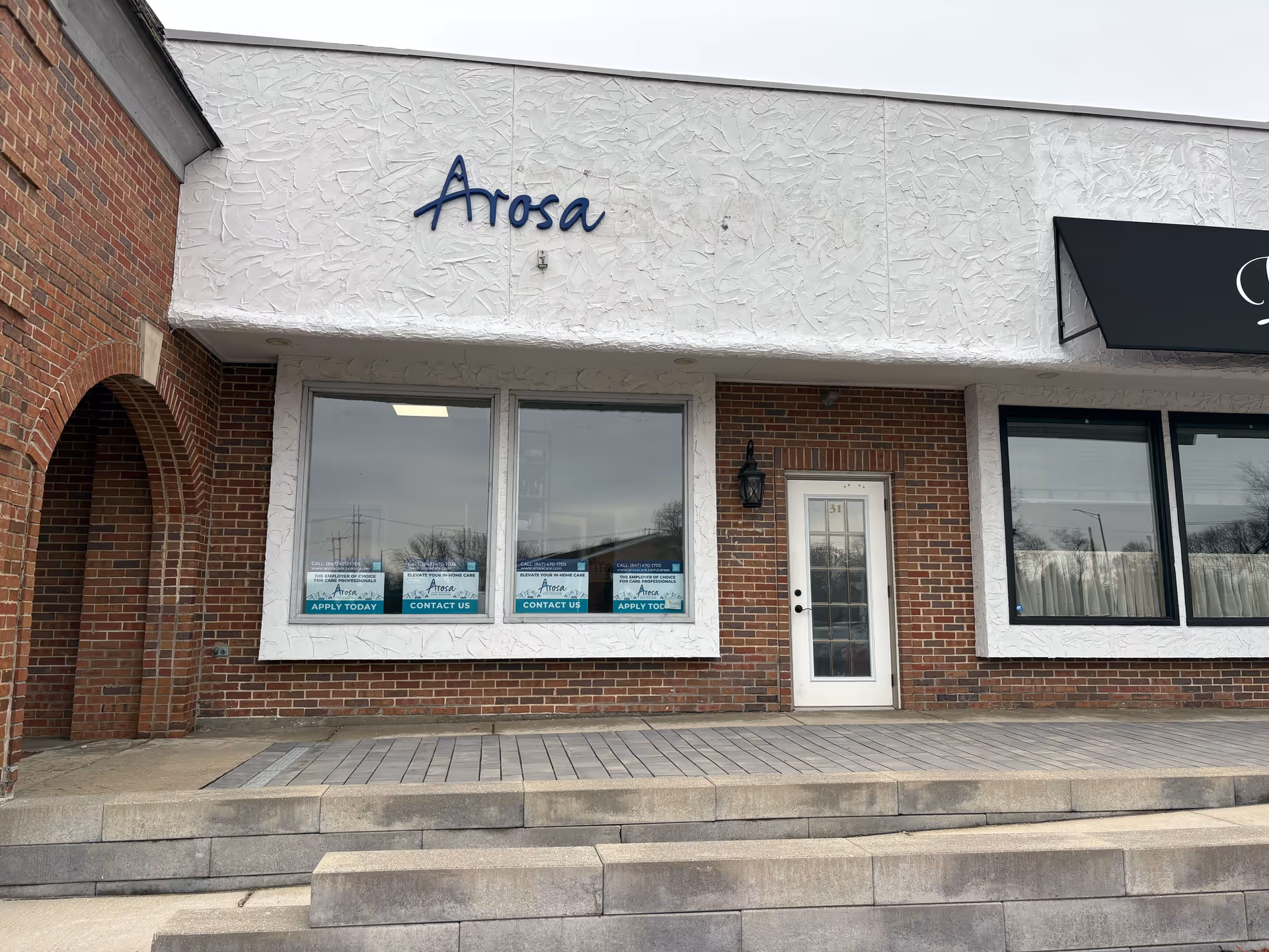 Brick storefront with Arosa sign, large windows, and a white entrance door.
