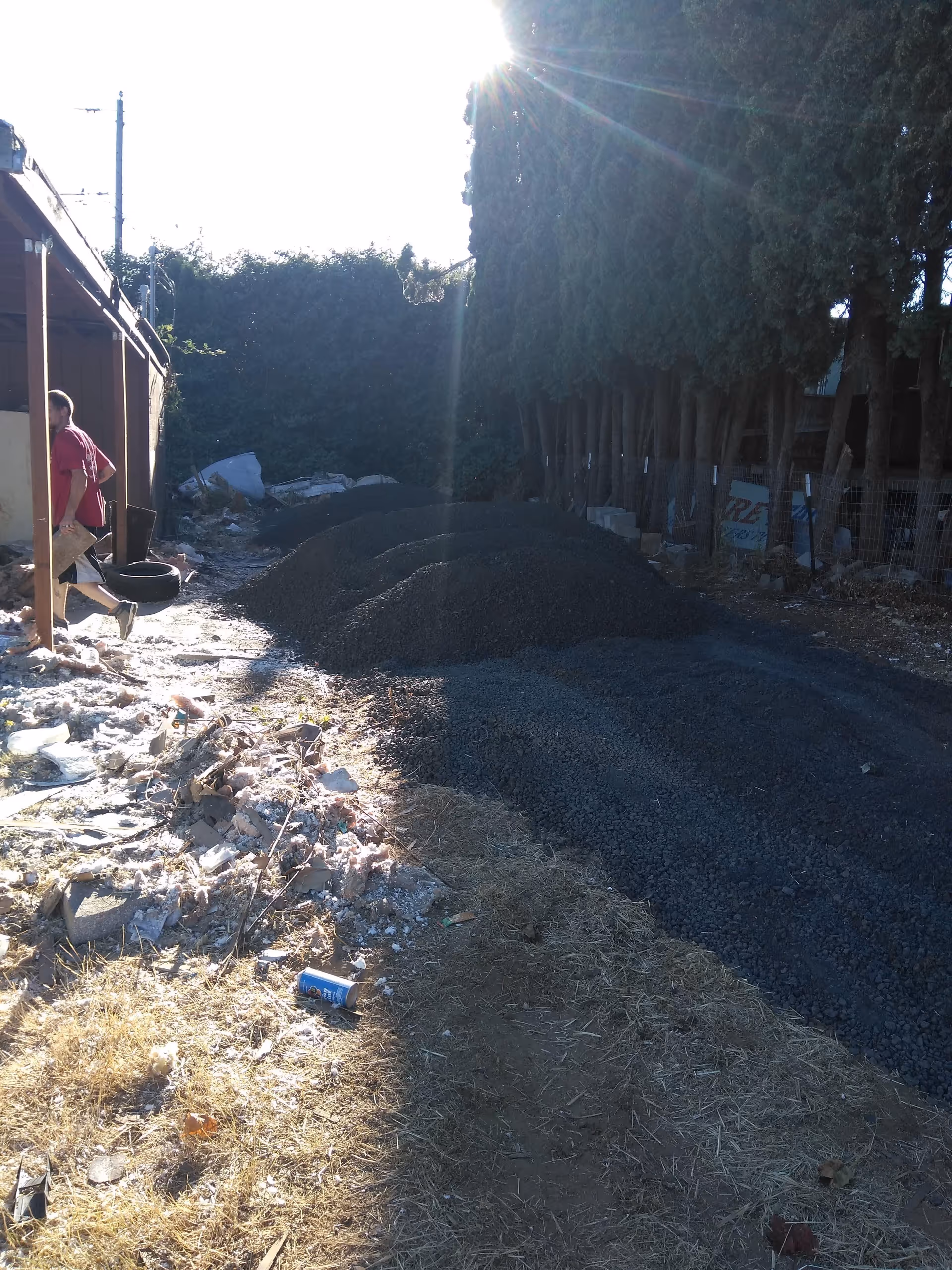 Outdoor construction site beside building with gravel piles and a person standing near debris.