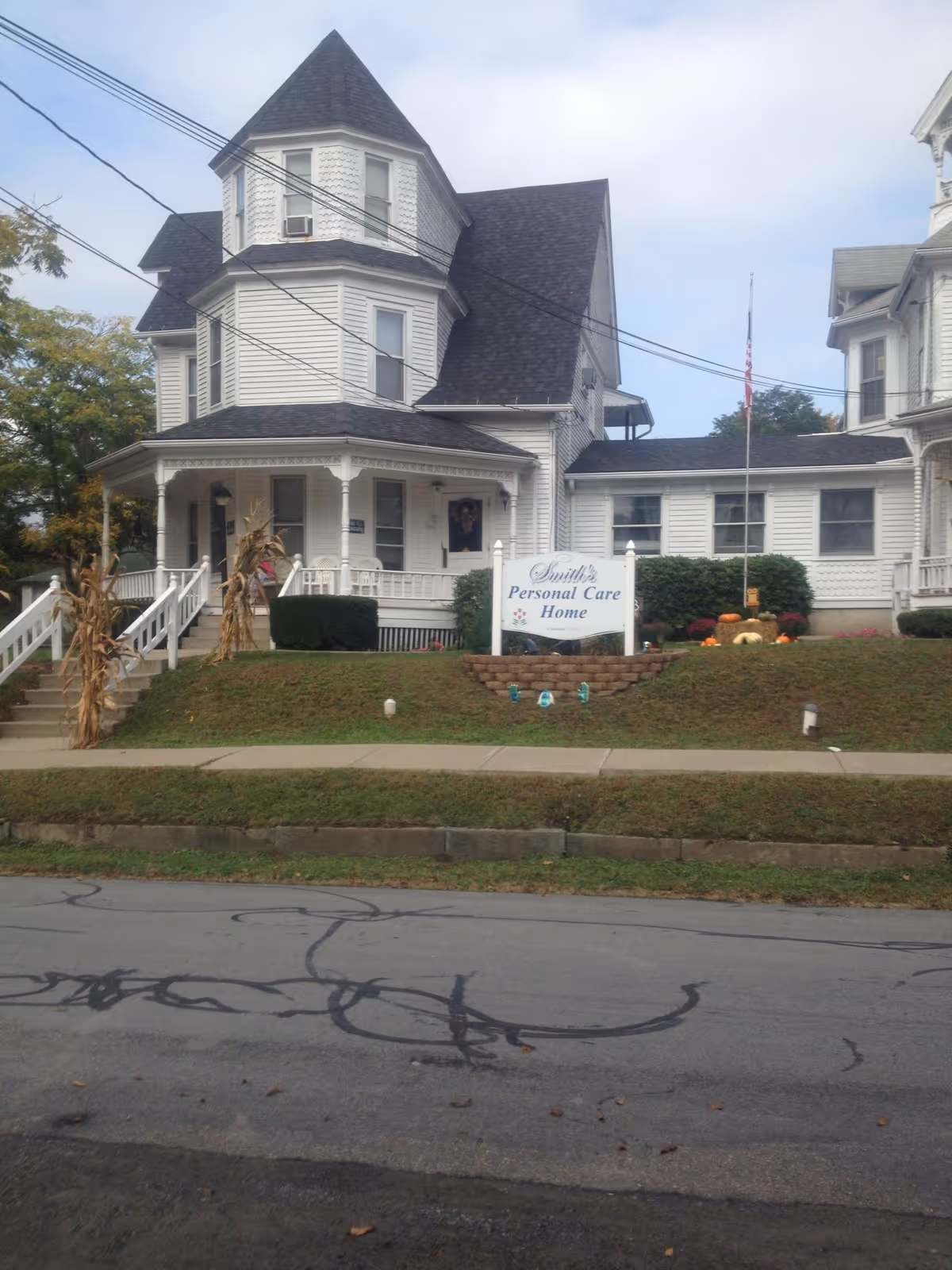White Victorian-style house with a sign reading Smith's Personal Care Home and autumn decorations.