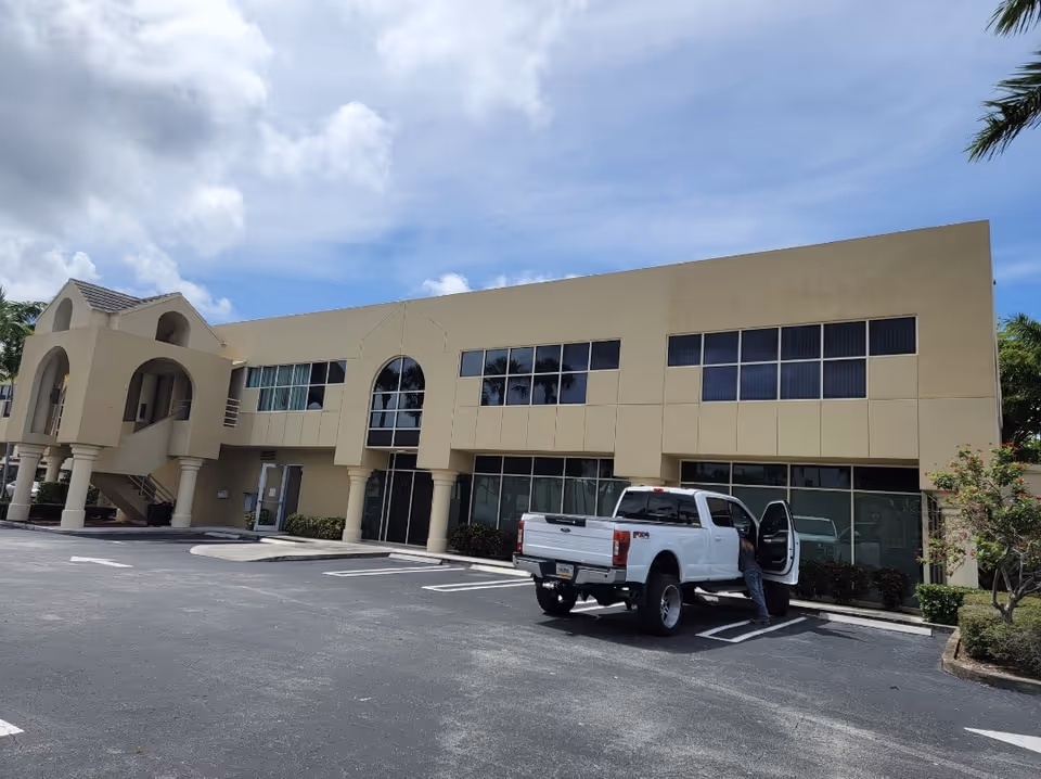 Two-story beige senior facility with arched entryway, large windows, and a white pickup truck.
