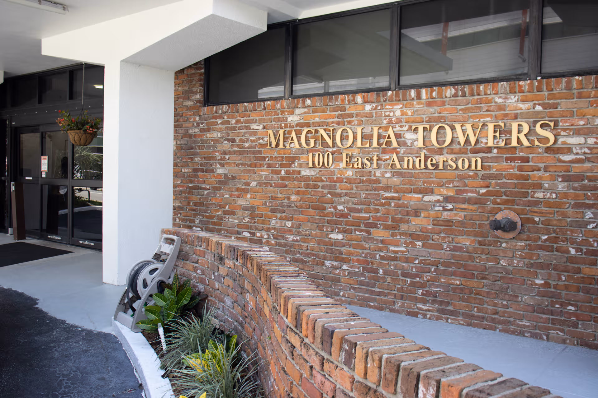 Exterior brick wall entrance of Magnolia Towers with signage and surrounding plants