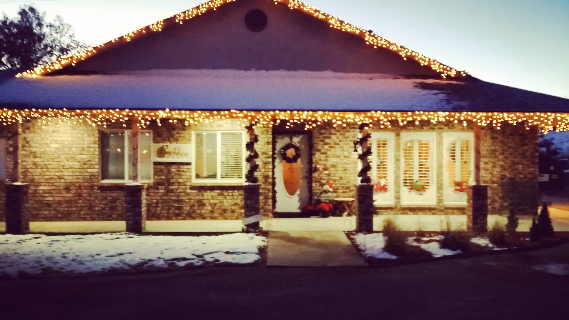 Brick assisted living front entrance decorated with Christmas lights and wreaths; patches of snow.