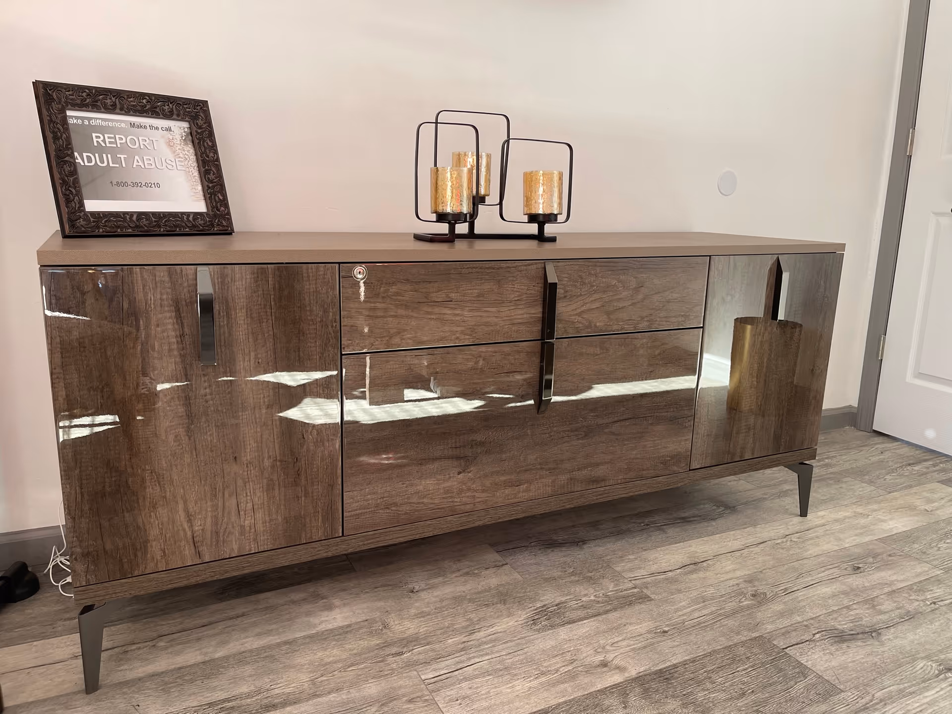Glossy wooden sideboard with framed sign and candle holders on top, against a light wall.