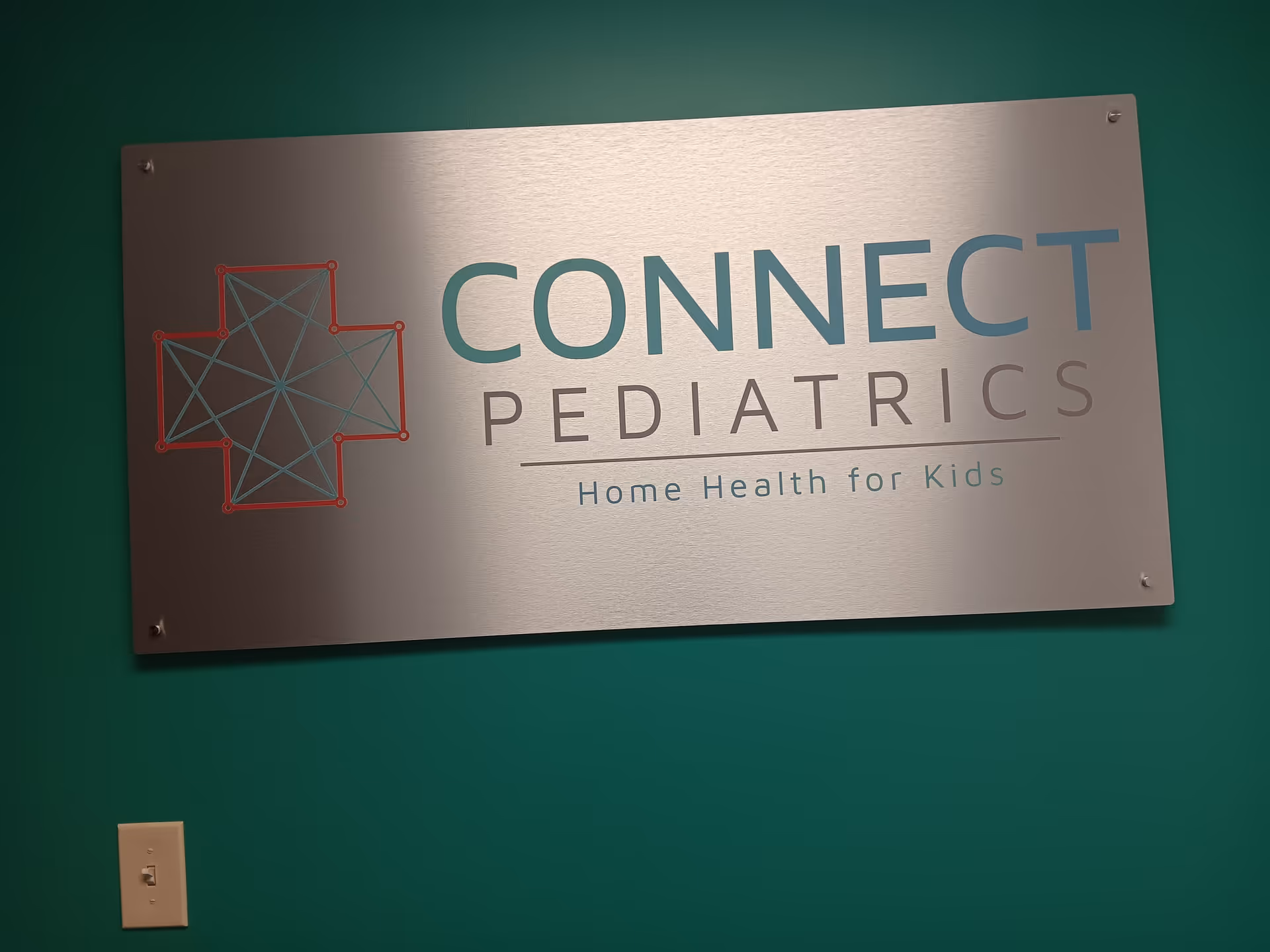 Metal sign on a teal wall reading CONNECT PEDIATRICS Home Health for Kids.