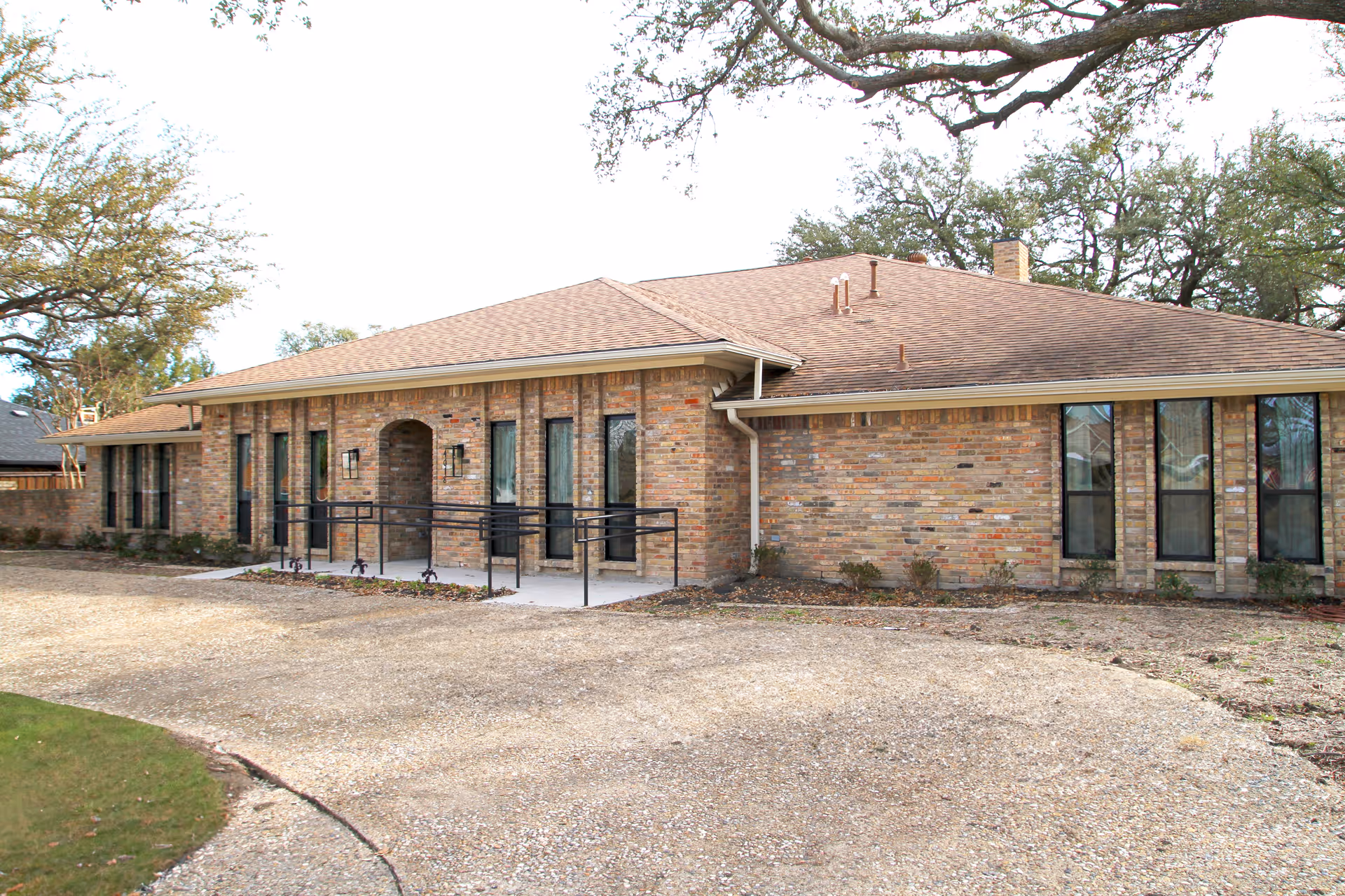 Single-story brick senior living facility with welcoming entrance and a gravel parking area.