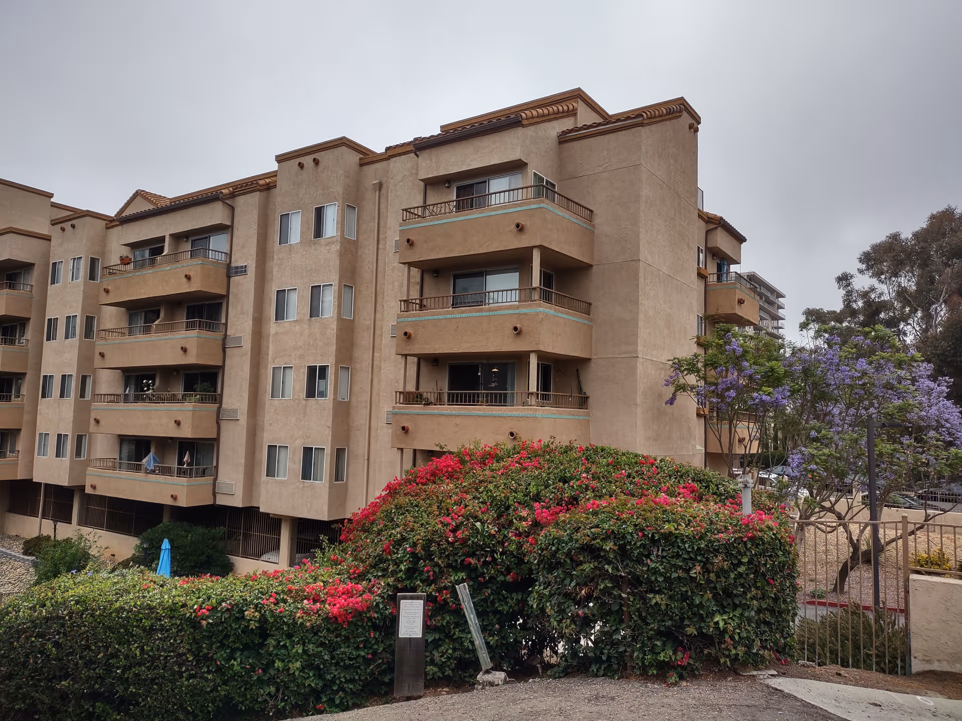 Exterior view of Villa Pacifica senior living building with balconies and flowering shrubs.