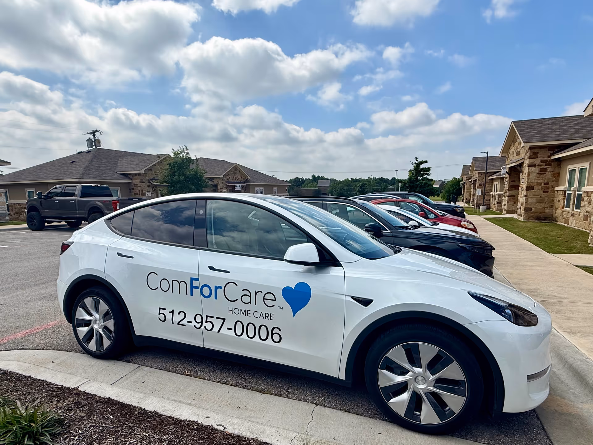 White ComForCare van parked in front of a stone building under a blue sky.