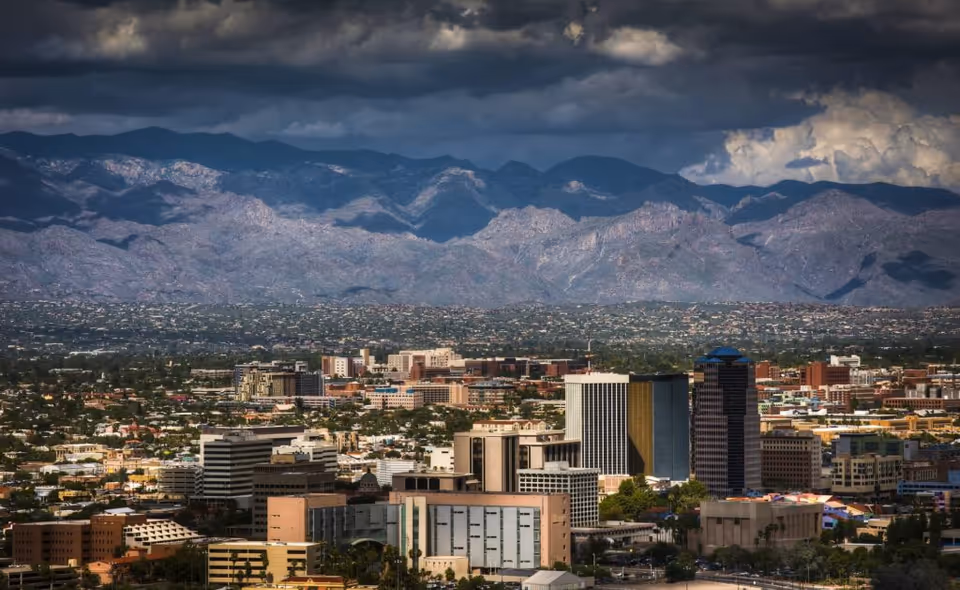 Wide cityscape of downtown skyline with distant mountains beneath dramatic clouds.