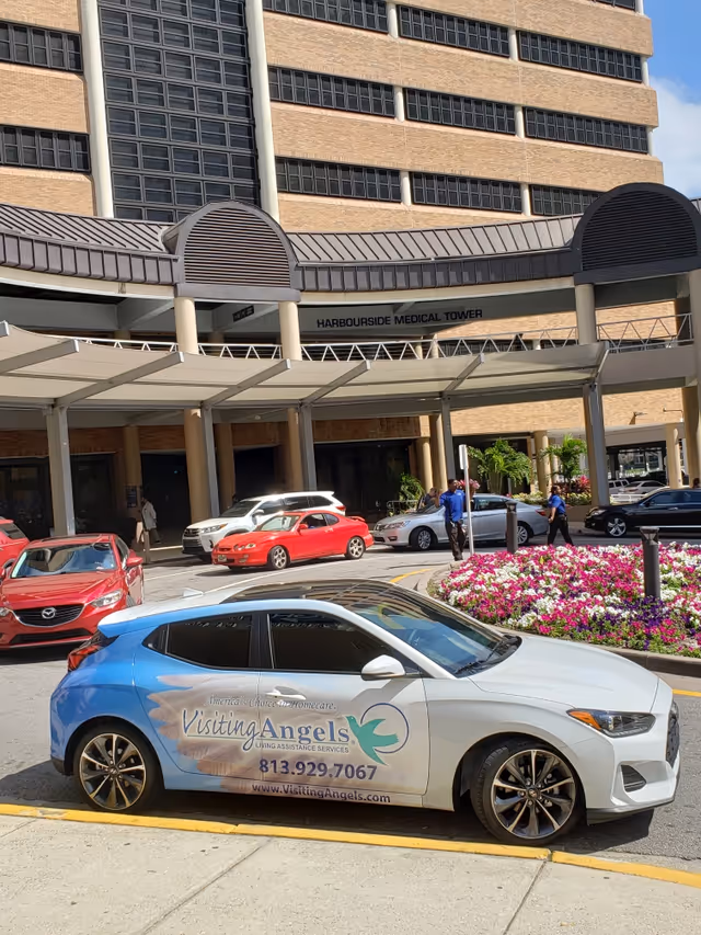 Exterior view of Harbourside Medical Tower with a Visiting Angels branded car in front.