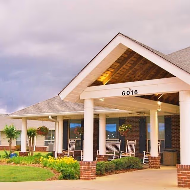 Exterior view of a senior living facility entrance with rocking chairs on a covered porch.