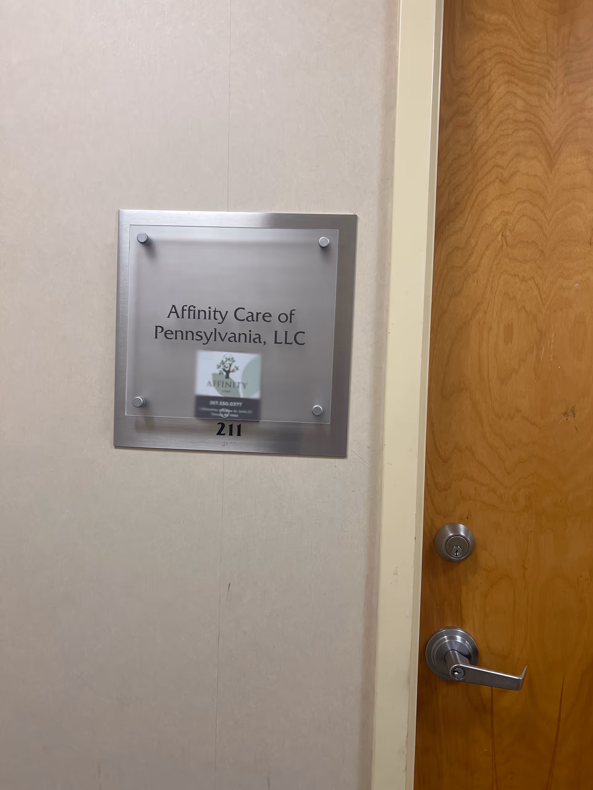 Affinity Care of Pennsylvania, LLC sign mounted on wall beside wooden door in hallway.
