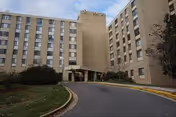 Front view of Sun Mar Nursing Center's multi-story exterior with entrance and curved driveway.