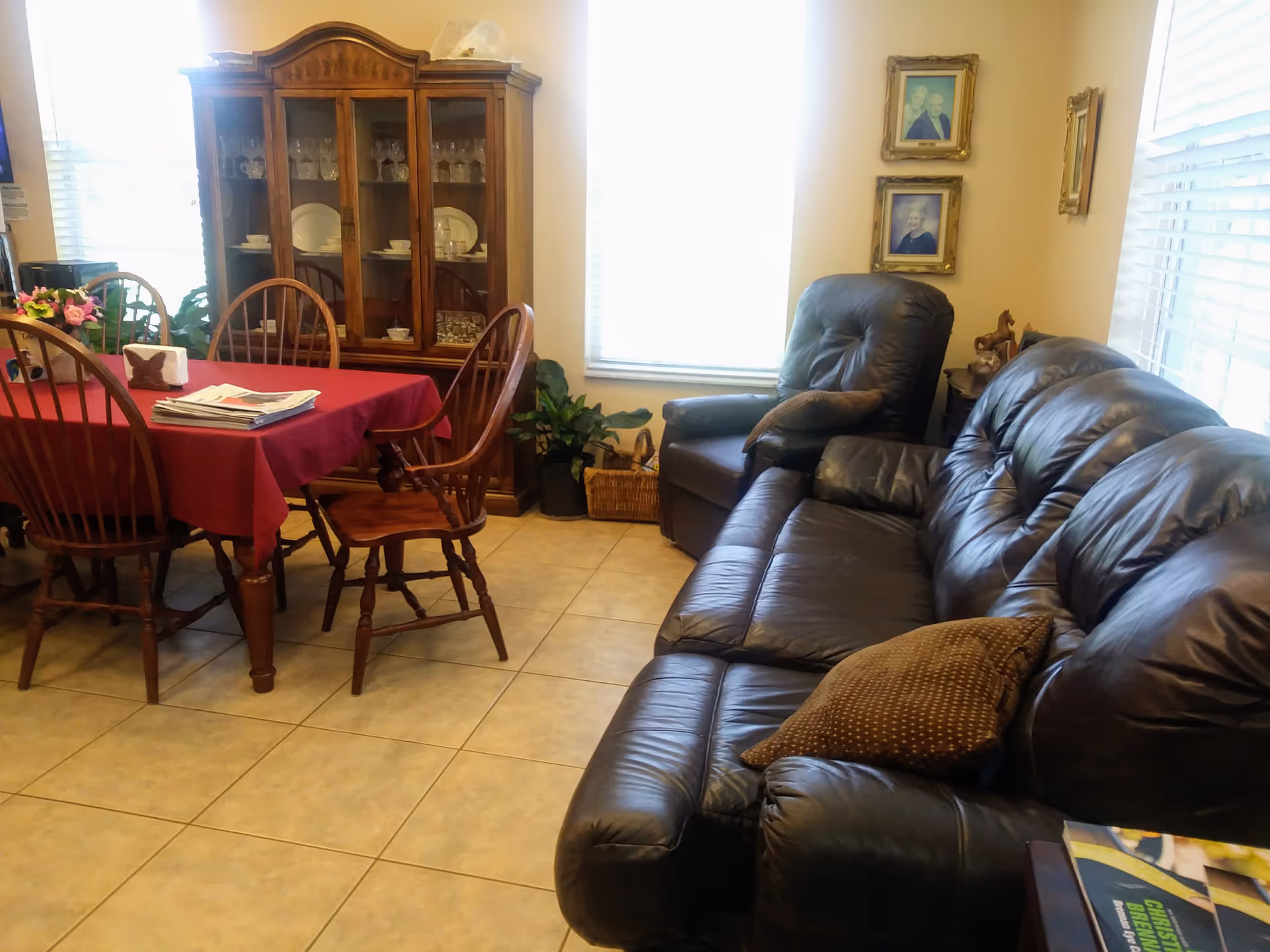 Cozy living area with dining table, china cabinet, and leather sofa in a sunny room.