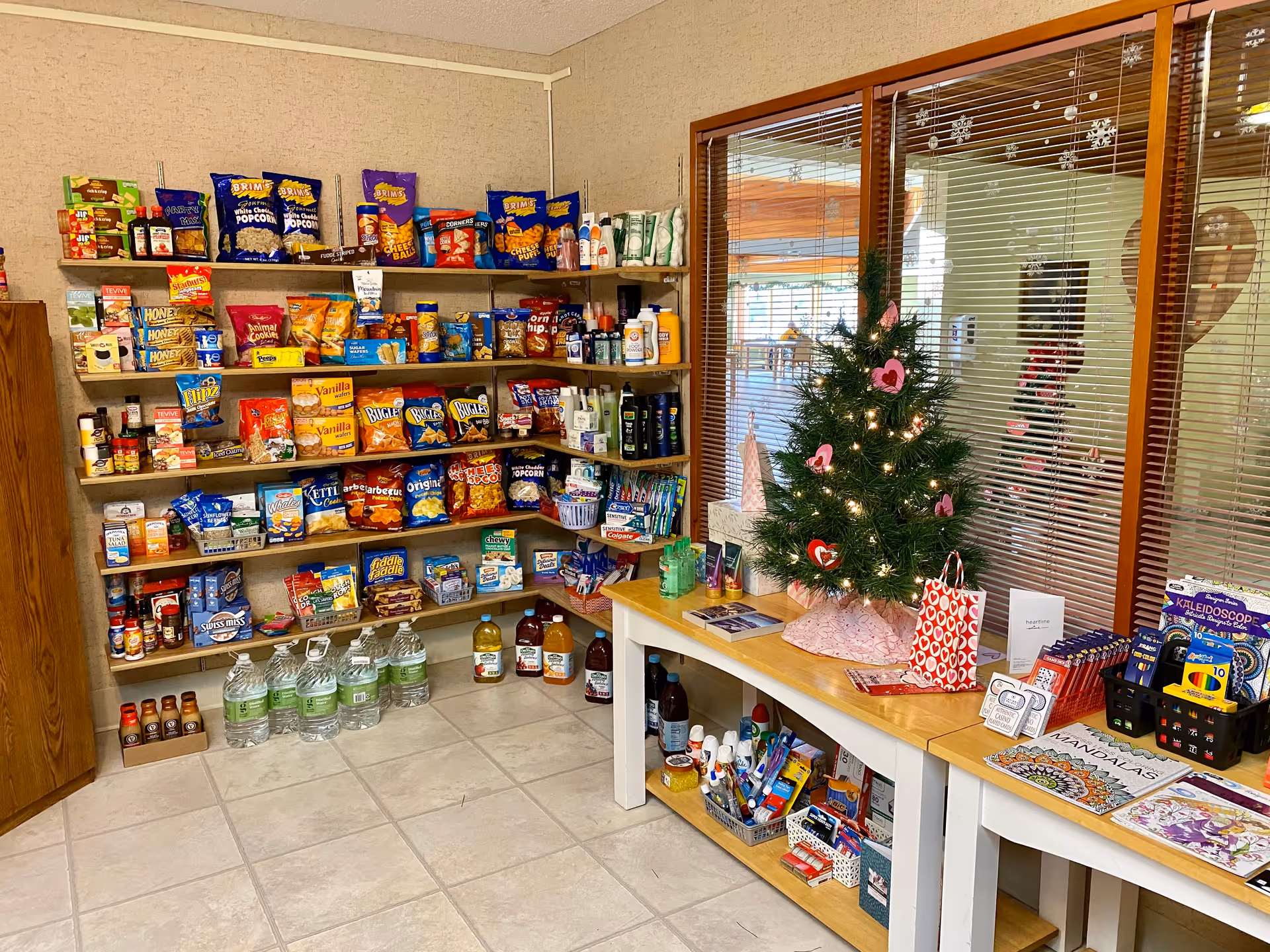 A snack pantry inside a senior living facility with shelves of chips and drinks, holiday tree.