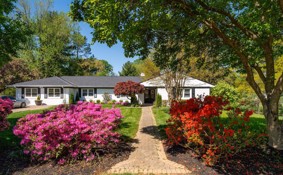 Single-story assisted living building with a stone path and vibrant flowering shrubs.