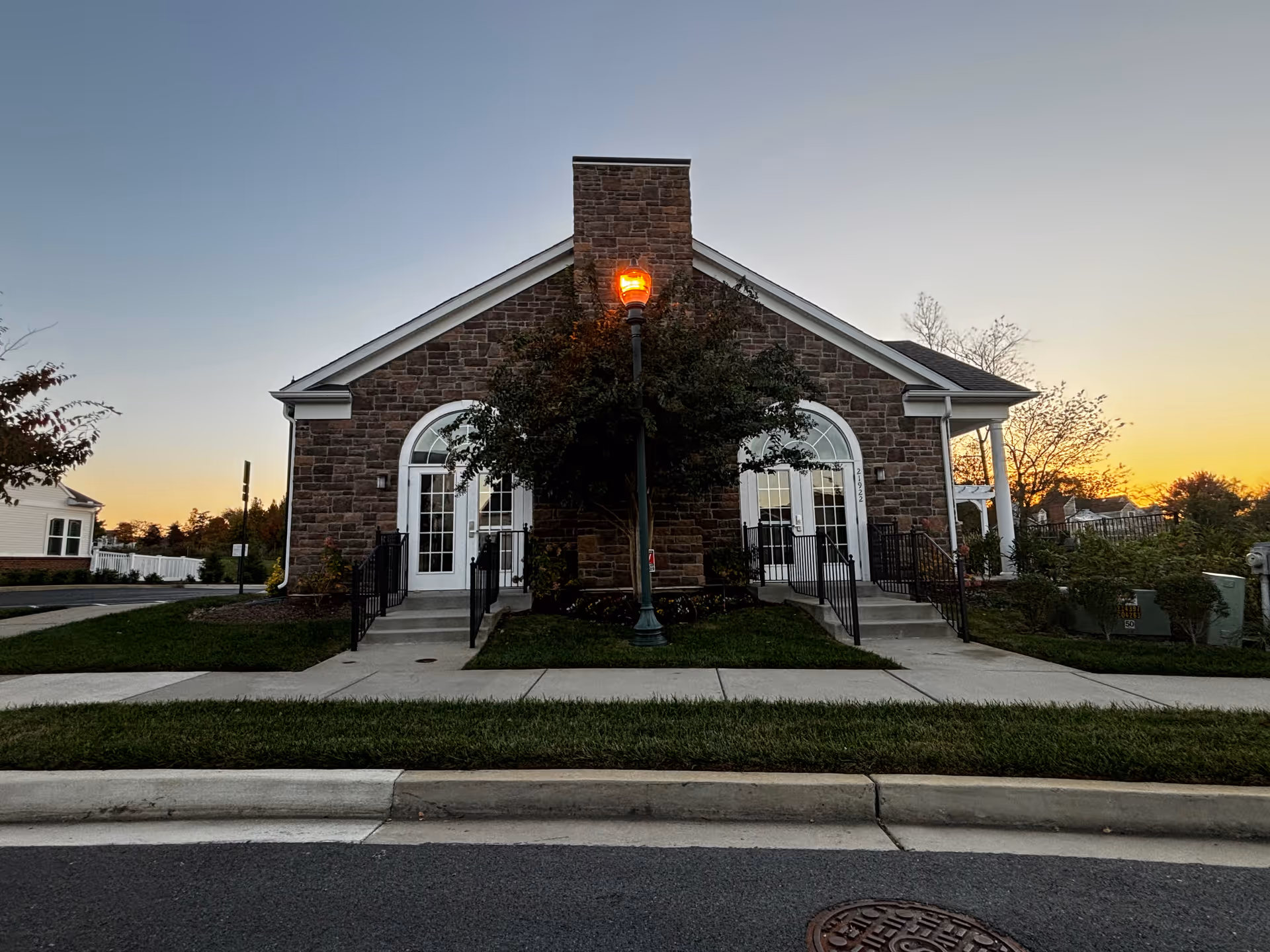Stone-front community building with two arched glass doors, a central lamppost, and walkways at sunset.