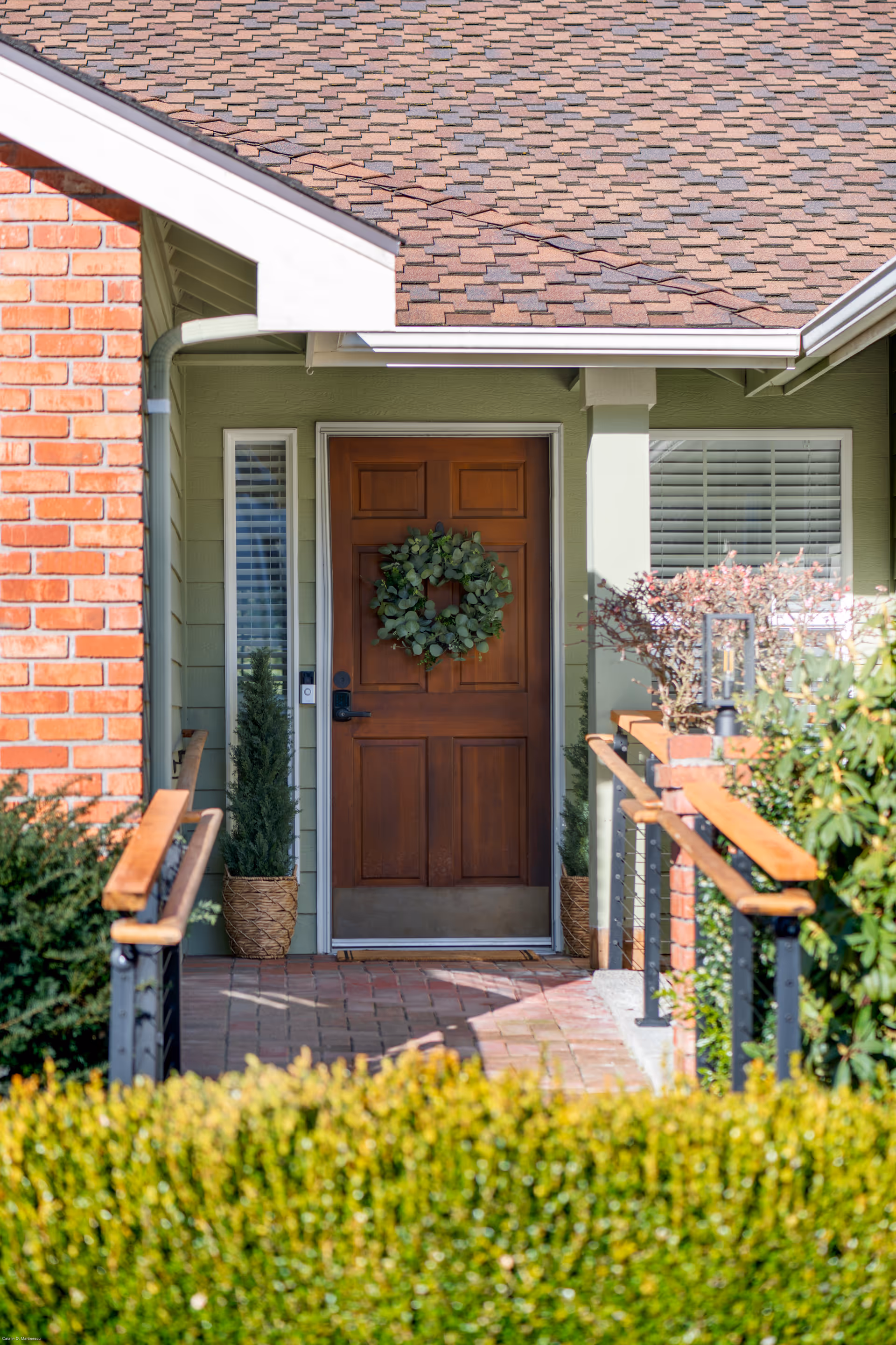 Wooden front door with a wreath, green siding, brick accents, and a brick path with railing.