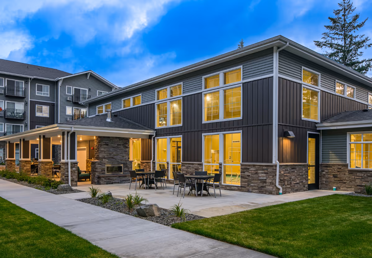 Modern senior living building with outdoor patio seating and stone accents, evening lighting.