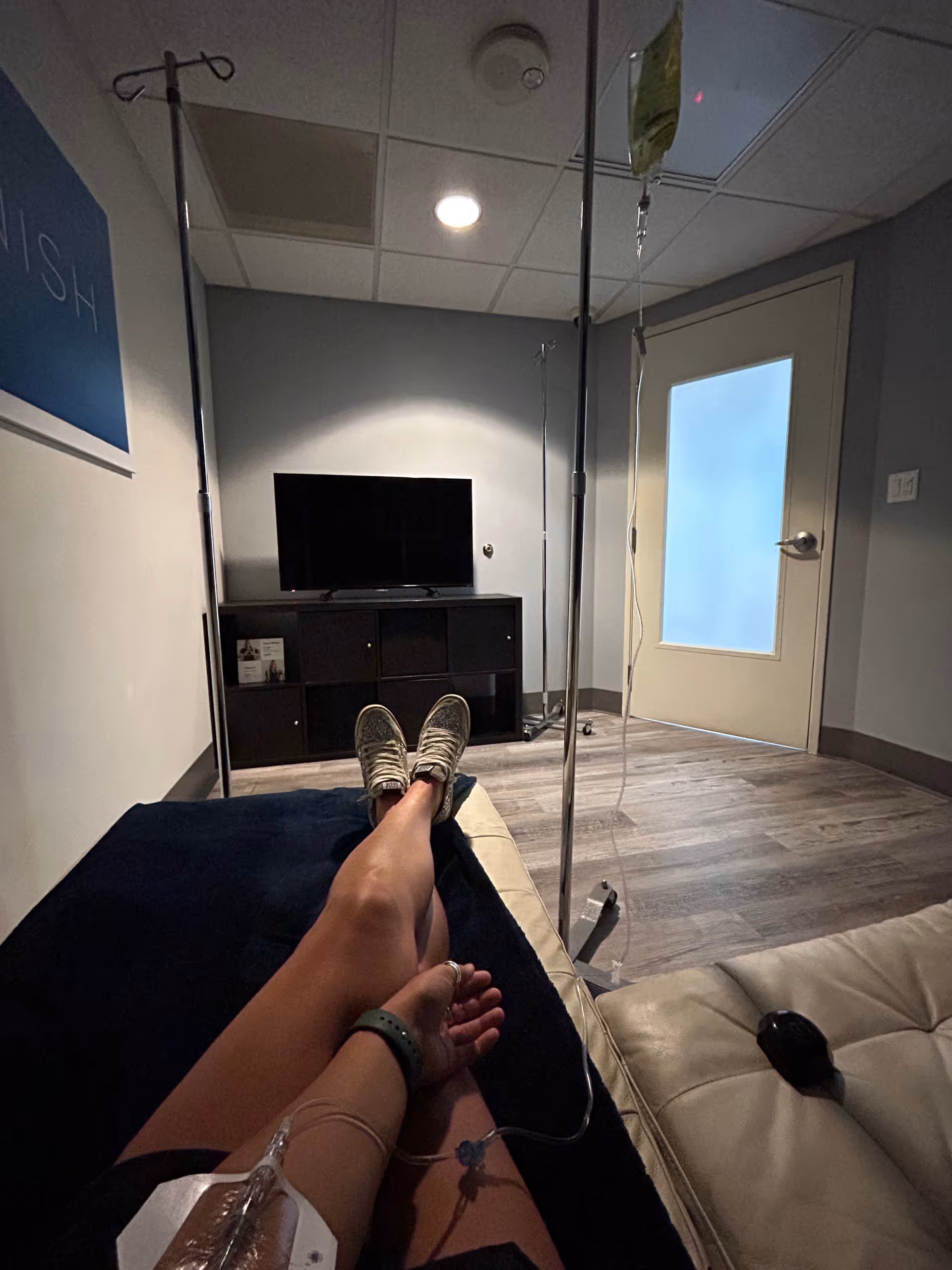 Patient reclining with IV therapy in a small lounge room, TV on a cabinet.