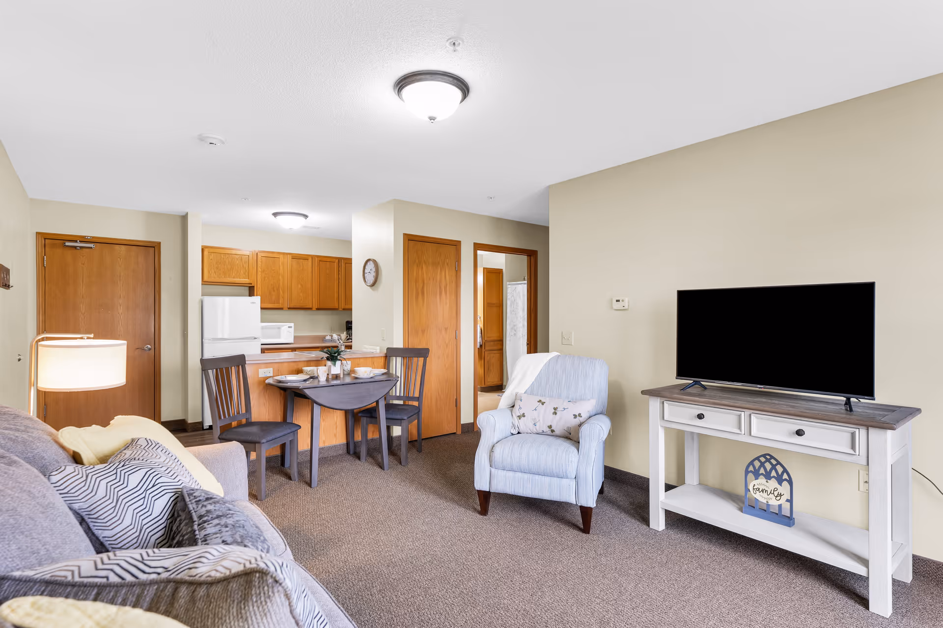 Living area with sofa, armchair, TV stand, dining table, and open kitchen.
