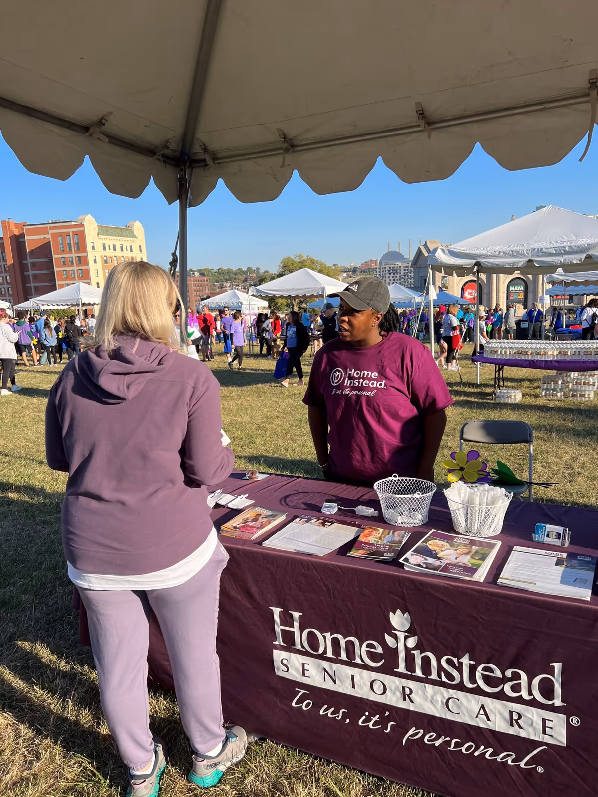 Outdoor community fair with Home Instead Senior Care booth and staff assisting attendees.