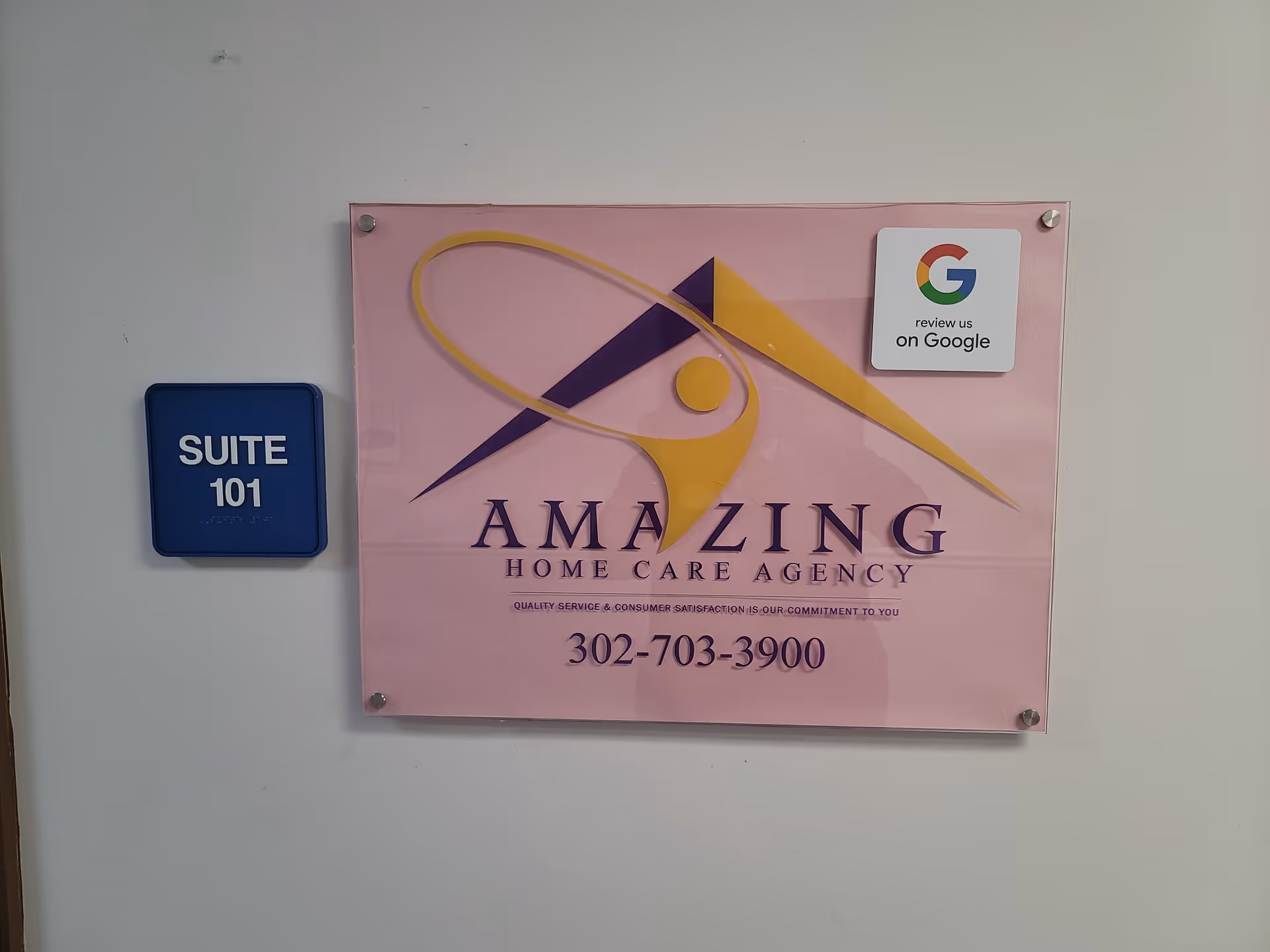 Pink sign reading Amazing Home Care Agency with suite plaque on a hallway wall.