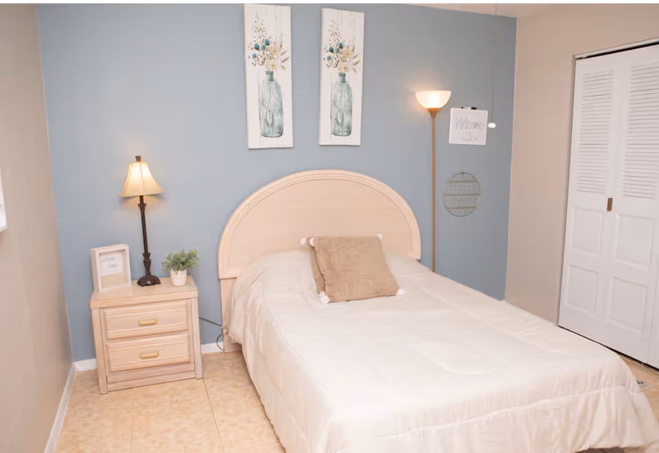 Cozy bedroom with a single bed, nightstand, lamp, and blue accent wall.