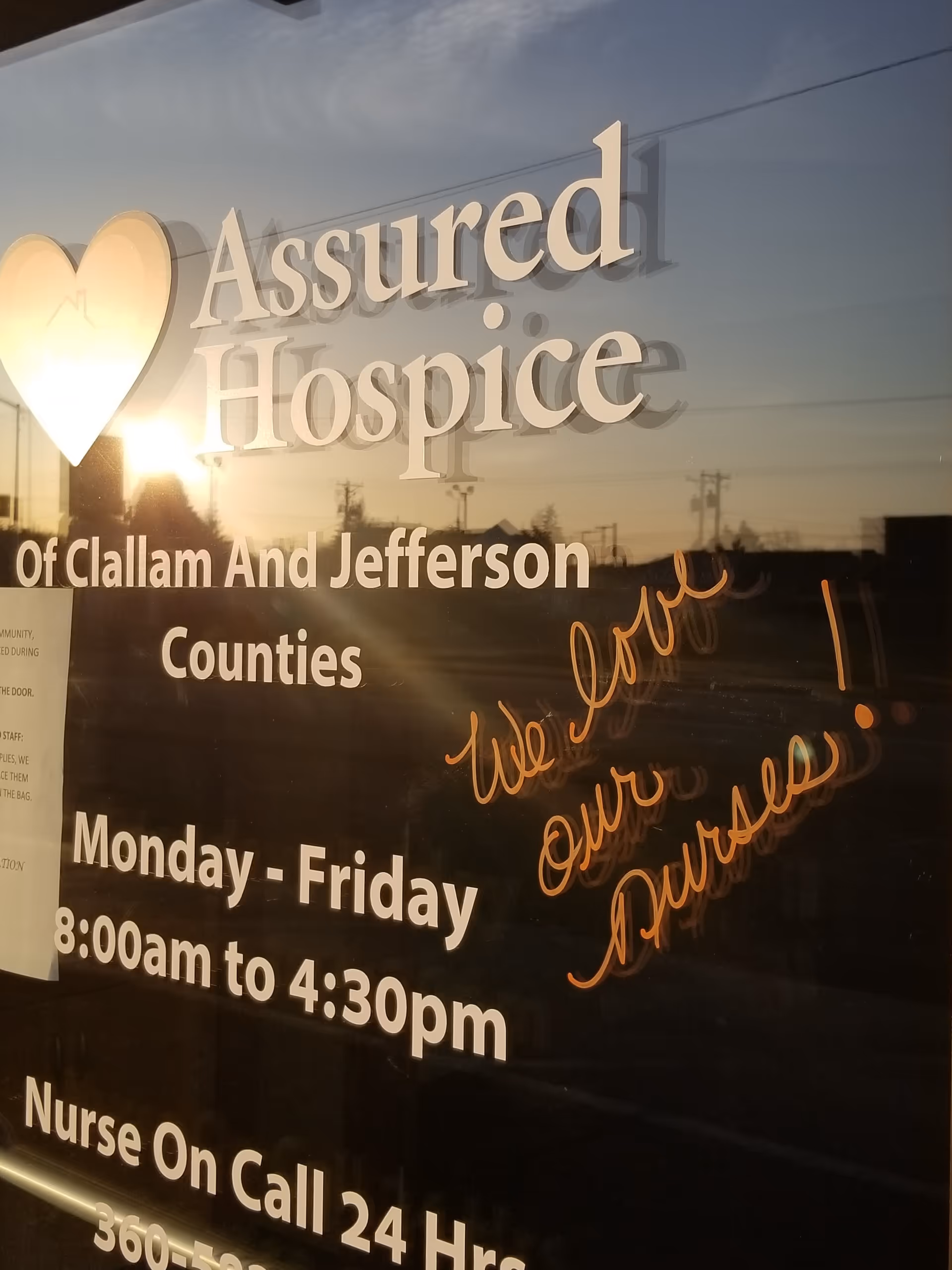 Glass storefront sign for Assured Hospice with street reflections.