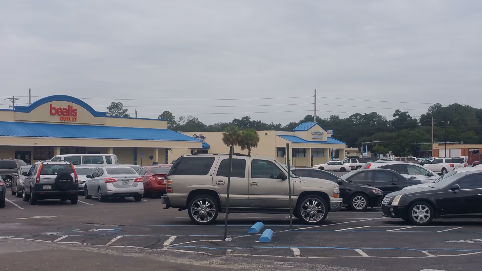 Exterior view of a shopping plaza with Bealls Outlet storefronts and parked cars.