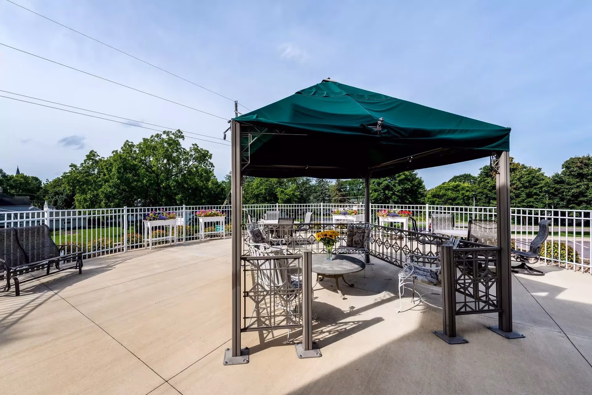 Outdoor terrace with a green canopy, metal seating, railing, and planters.