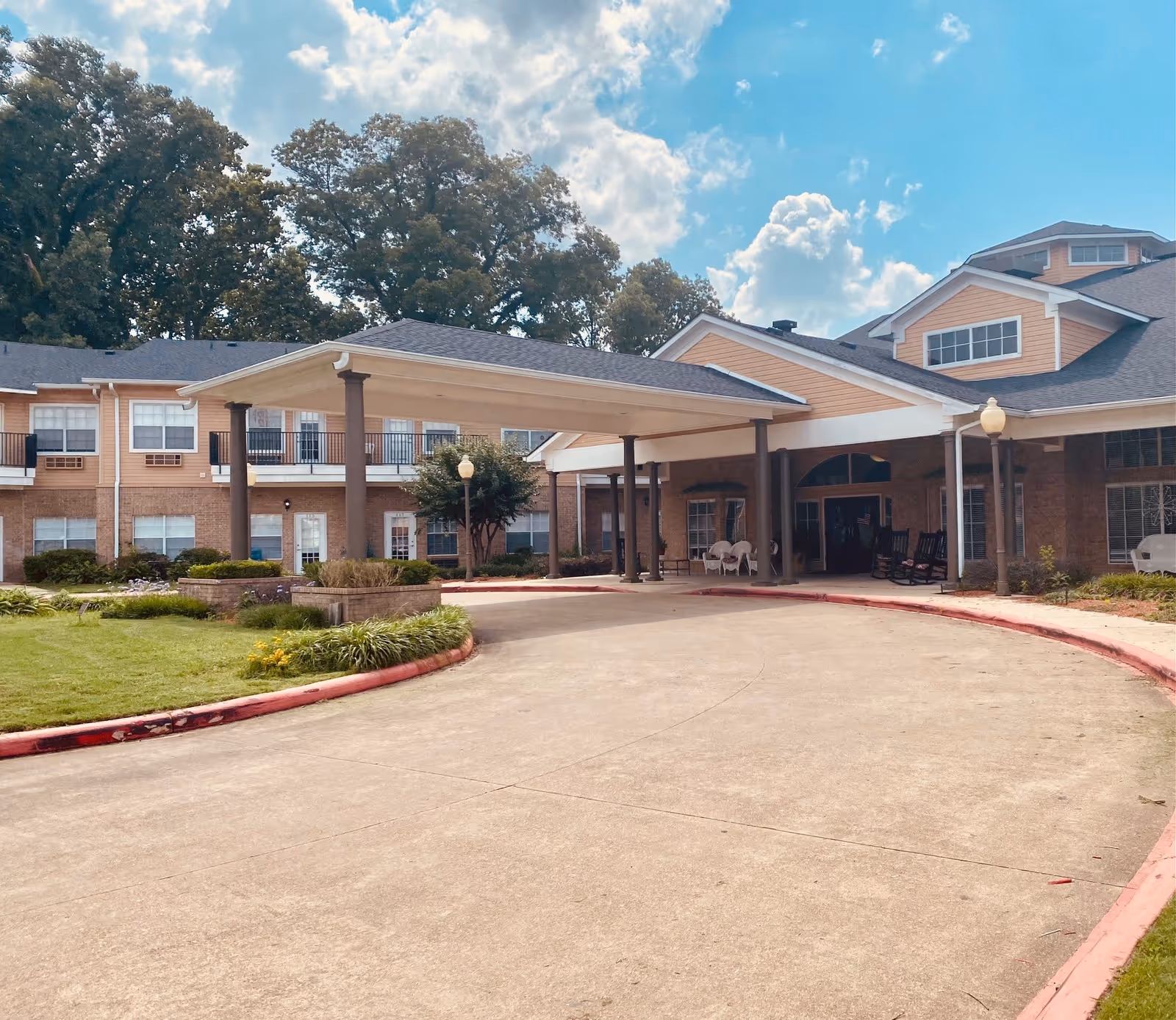 Front exterior view of Brookdale Waterview Court senior living facility showing a covered entrance with columns, a curved driveway, landscaped greenery, and a partly cloudy sky.
