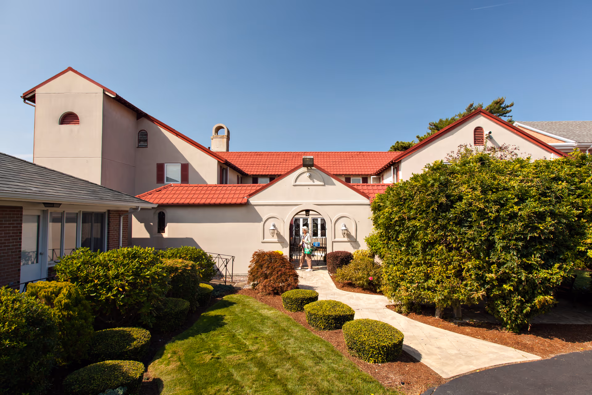Exterior view of Royal Cape Cod Nursing and Rehabilitation Center with red-tiled roof and landscaped grounds.