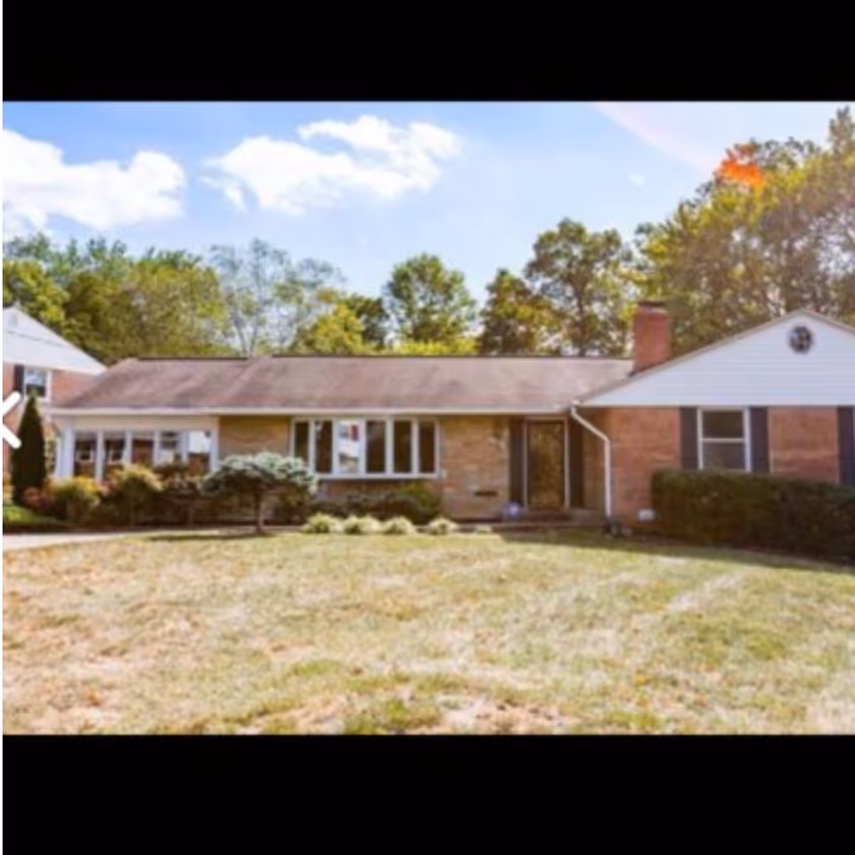 Single-story brick ranch-style house with a front lawn, shrubs, and trees in the background.