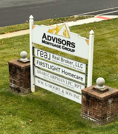 Outdoor signboard on a grassy lawn advertising FirstLight Homecare among other businesses.