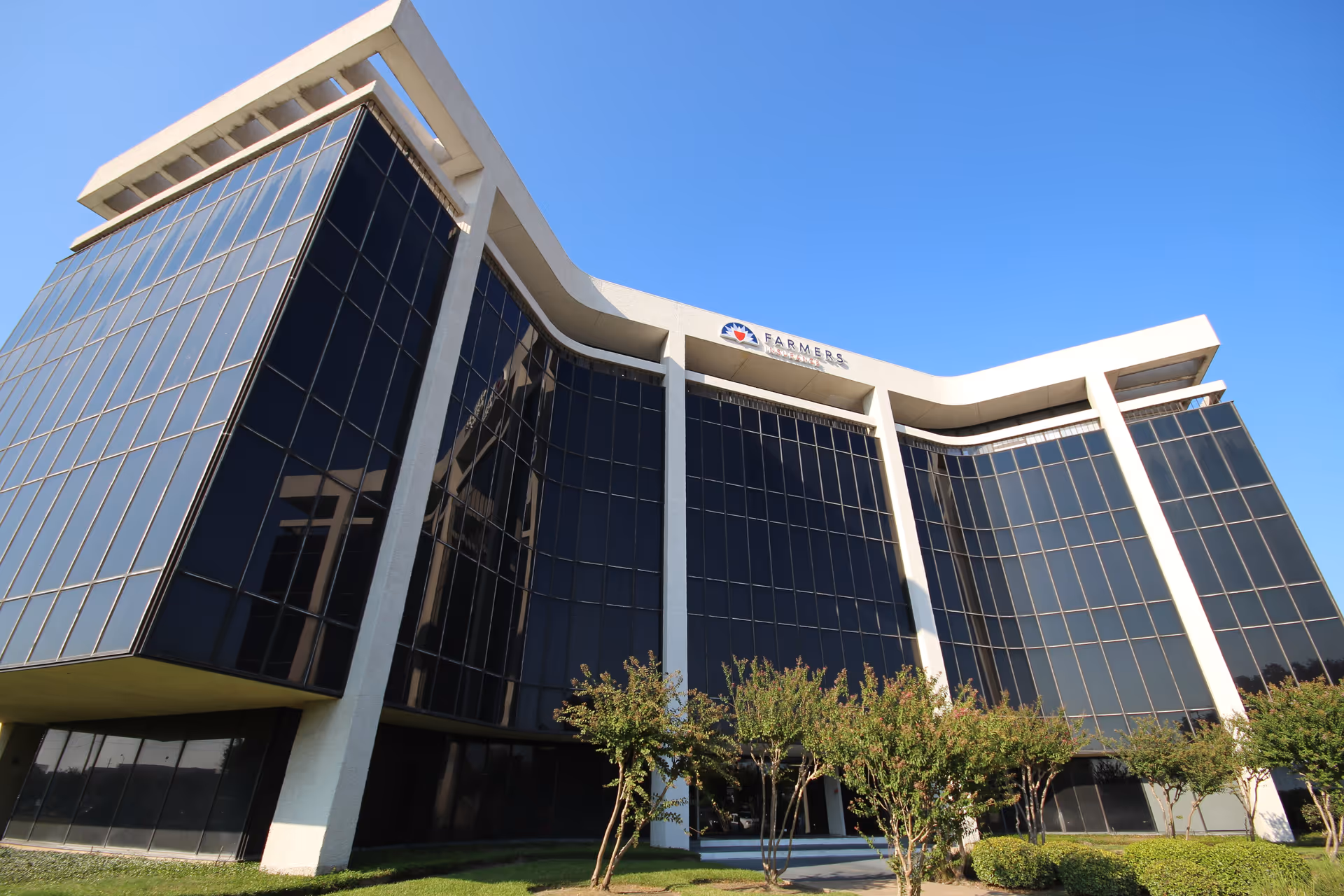 A modern glass-front building with curved white supports under a clear blue sky.