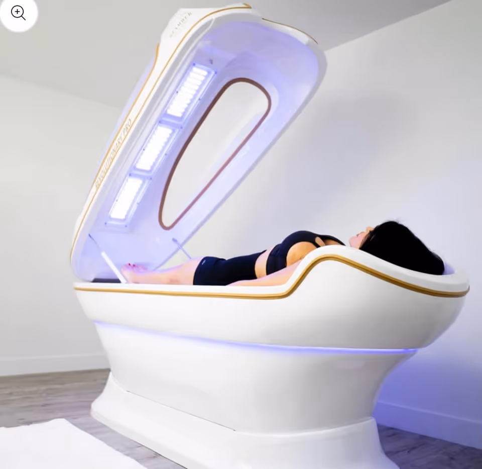 A person lies on a futuristic, illuminated medical spa bed in a bright room.
