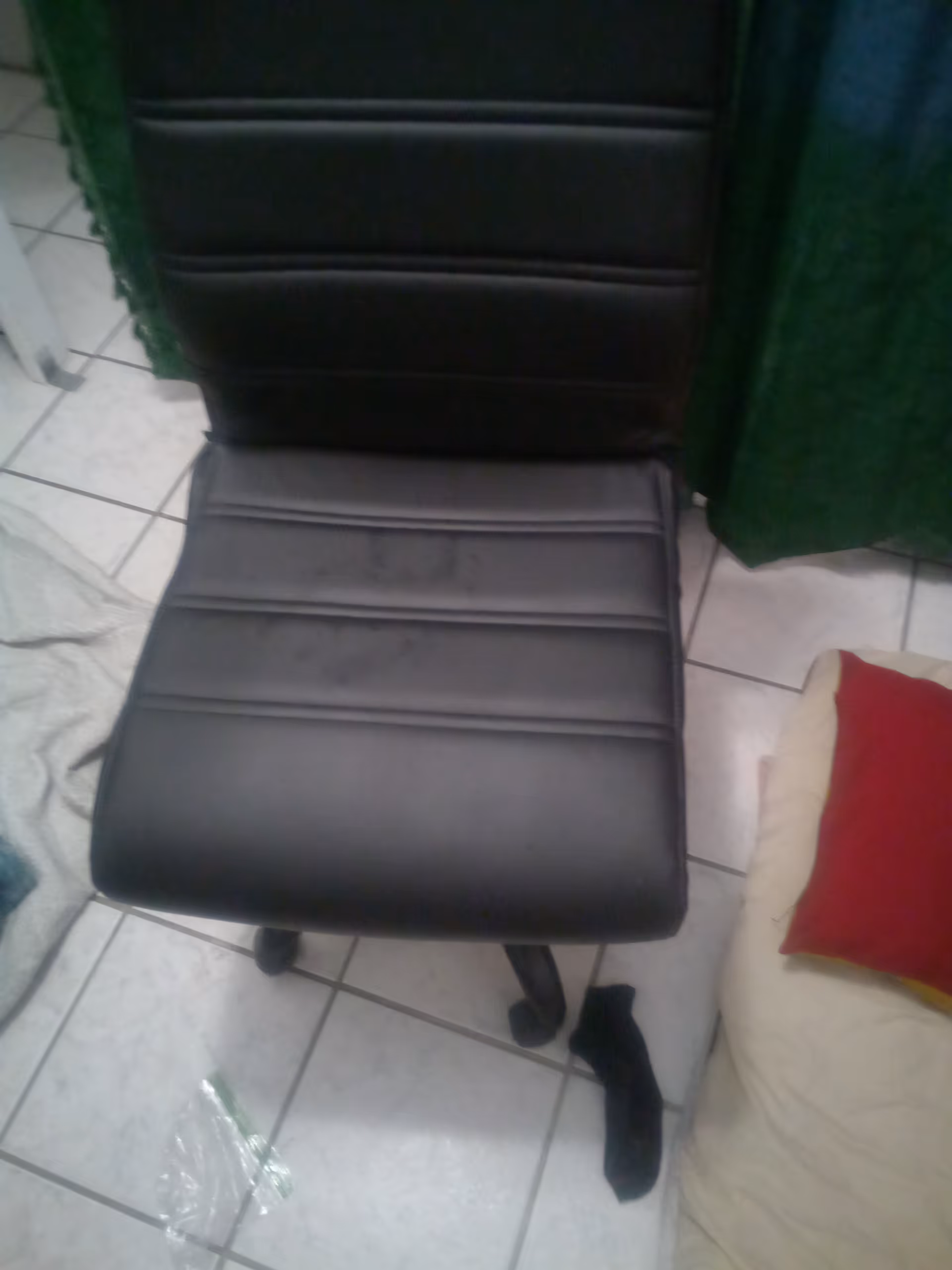 Black padded office chair on tiled floor beside a cream sofa with a red pillow.