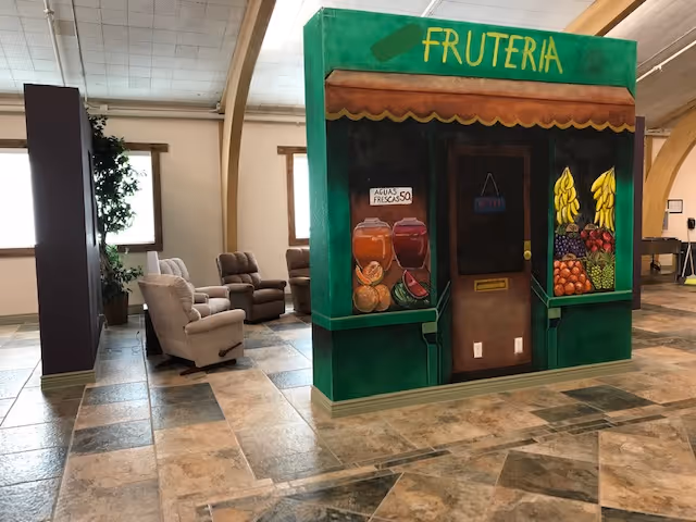 Interior common area featuring a painted 'Fruteria' mock storefront, tiled floor, and several recliner chairs.