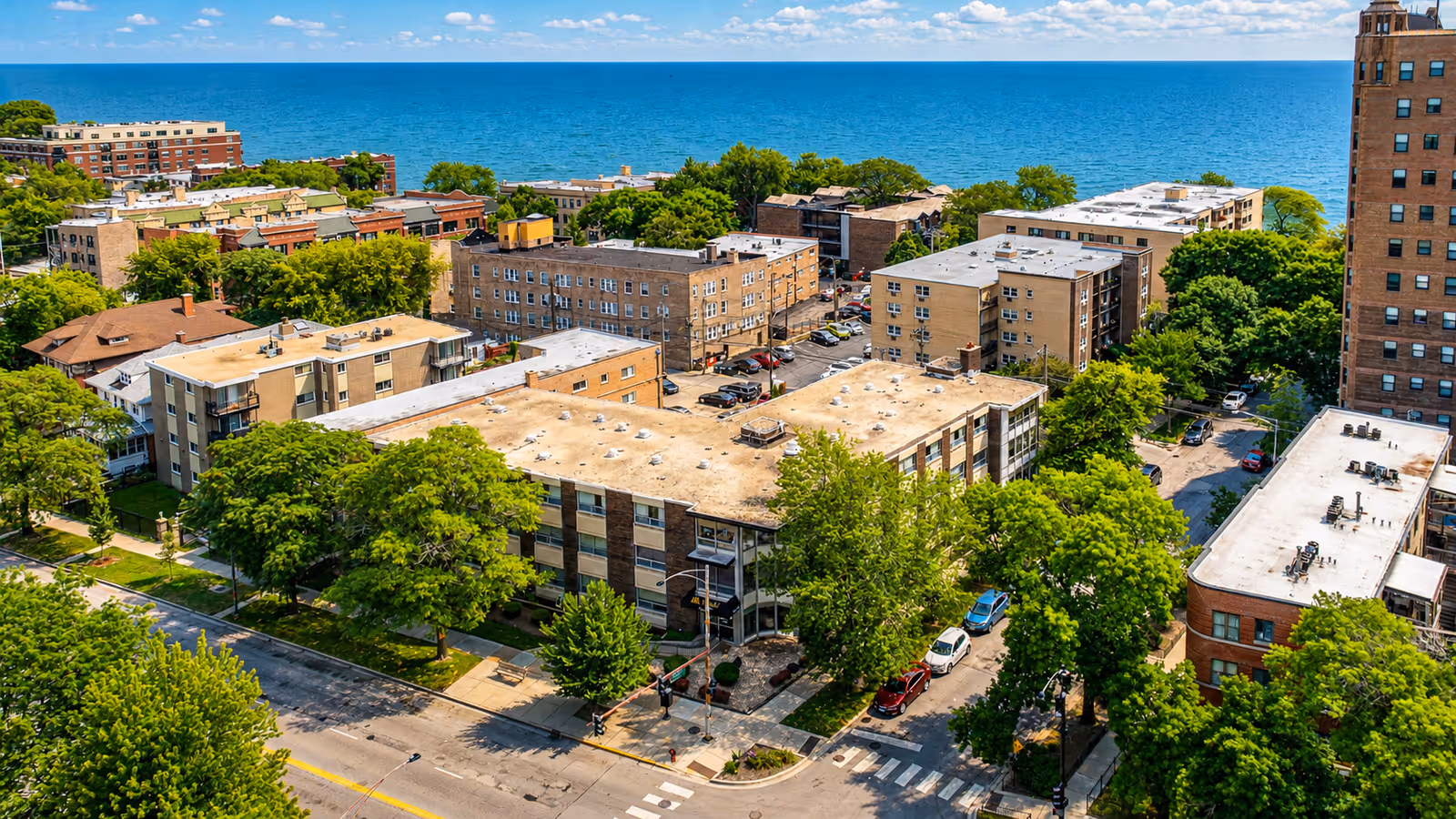 Aerial view of a waterfront urban neighborhood with mid rise buildings, streets, and abundant green trees.