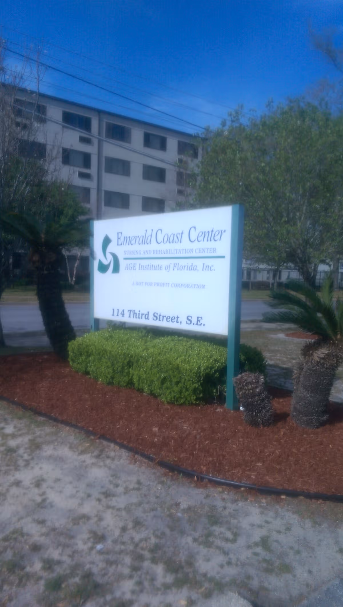 Exterior view of Emerald Coast Center sign with building and landscaping.