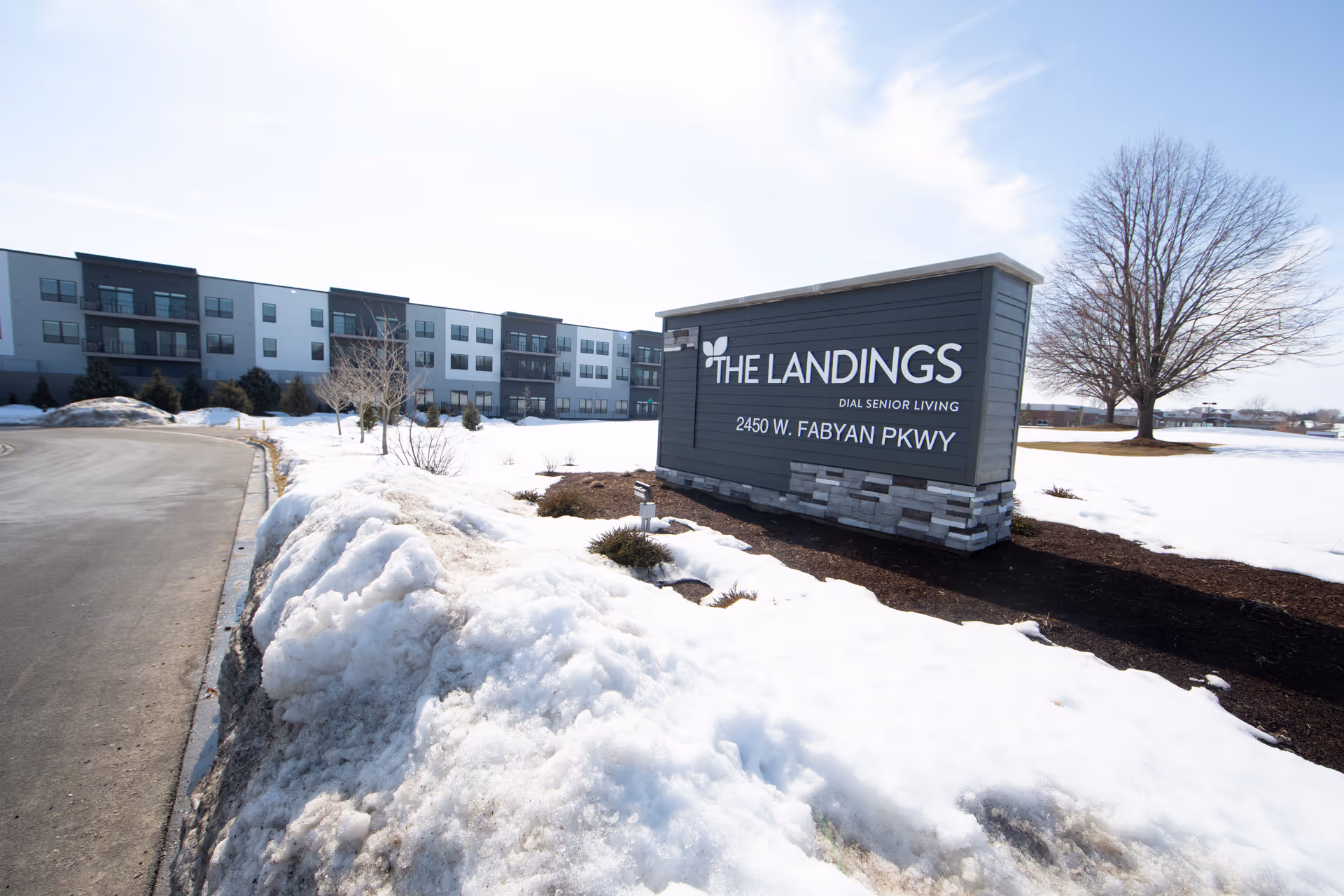 Entrance sign reading 'The Landings' with snow-covered grounds and the senior living building visible in the background.