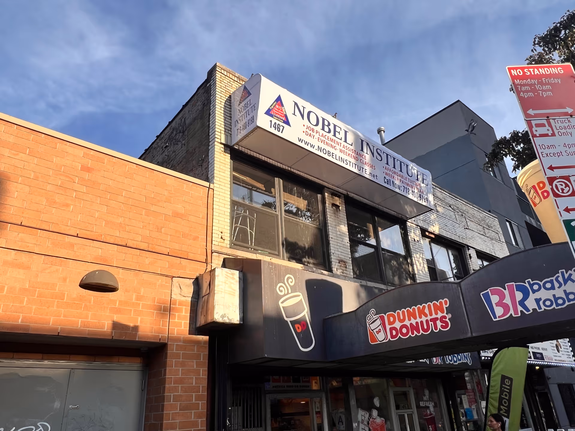 Two-story brick building with Nobel Institute banner, Dunkin’ Donuts signage, and street signs.