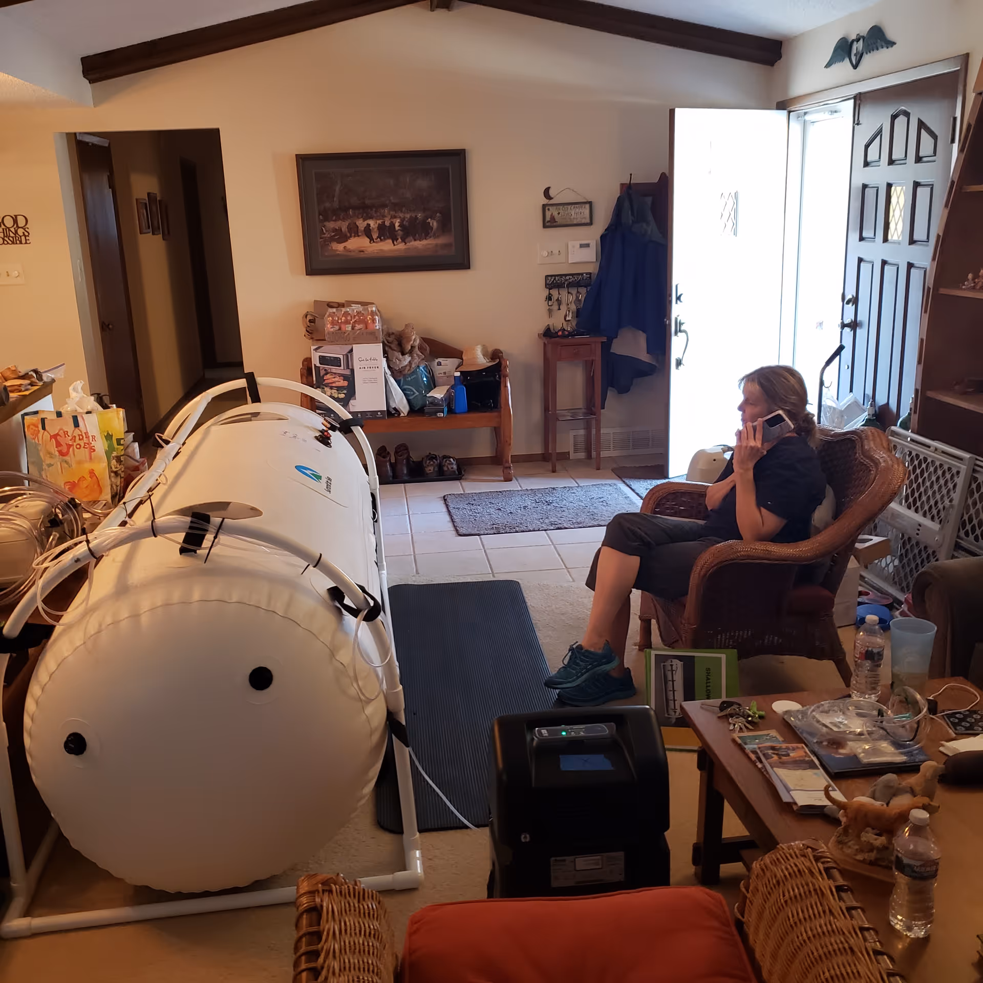 Person sits in a living room chair beside a large hyperbaric chamber.