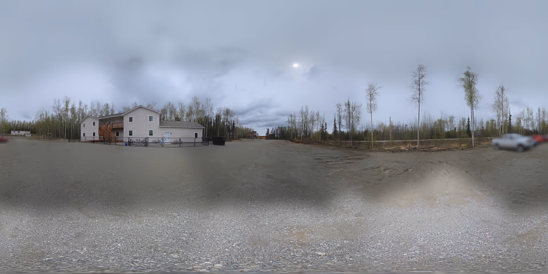 Wide exterior view of a modern two-story facility with a gravel lot and trees