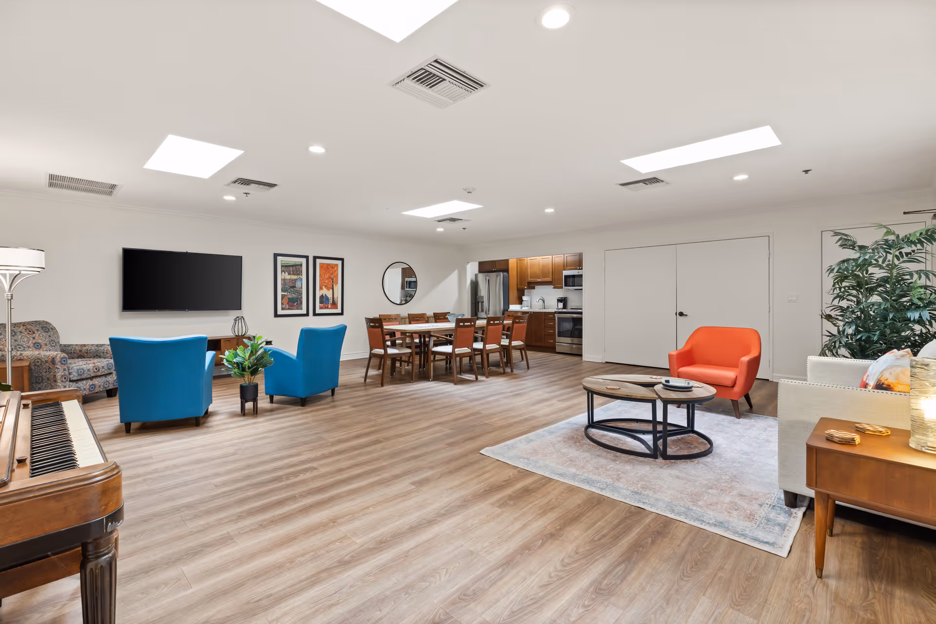 Spacious senior living lounge with colorful seating, television, and a dining area.