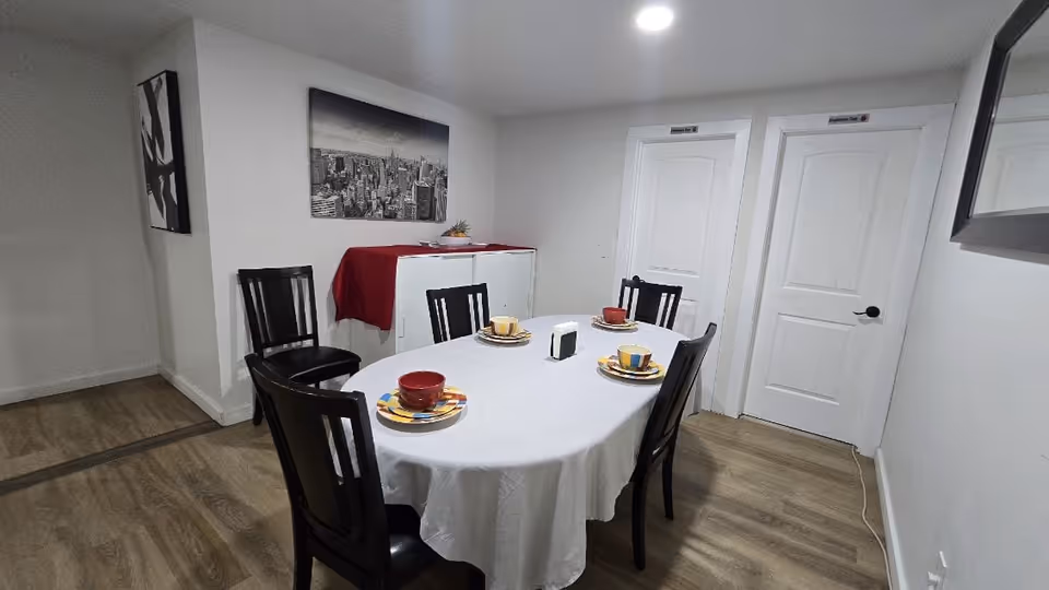 Round dining table with colorful dishware and chairs in a bright white dining room.